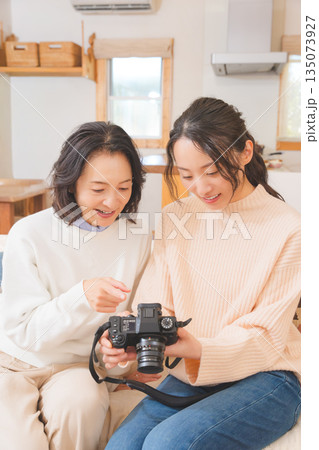 リビングで写真を見ながら旅行の思い出を楽しく話す母と娘 リビングで写真を見ながら旅行の思い出を楽しく話す母と娘 135073927