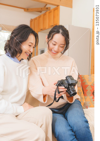 リビングで写真を見ながら旅行の思い出を楽しく話す母と娘 リビングで写真を見ながら旅行の思い出を楽しく話す母と娘 135073931