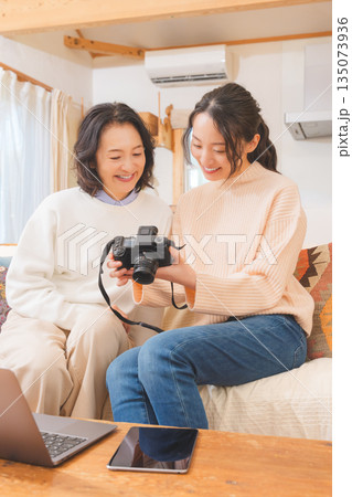 リビングで写真を見ながら旅行の思い出を楽しく話す母と娘 リビングで写真を見ながら旅行の思い出を楽しく話す母と娘 135073936