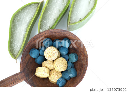 Natural aloe vera slices and colorful pills in a wooden spoon on white background 135073992