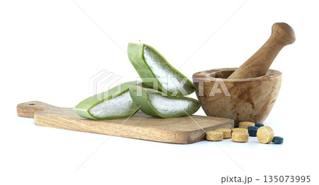 Fresh aloe vera slices and herbal supplements with mortar and pestle on a wooden board Fresh aloe vera slices and herbal supplements with mortar and pestle on a wooden board 135073995