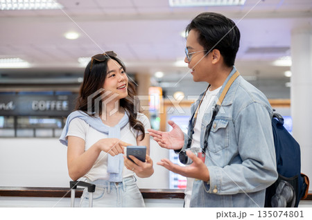 Asian tourist couple go on trip a woman holding phone and talking to a man while standing in airport Asian tourist couple go on trip a woman holding phone and talking to a man while standing in airport 135074801