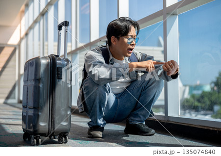 Frustrated asian man crouching looking at time on watch running late or missed a flight in airport 135074840