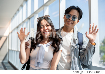 Happy asian tourist couple go on a trip man and woman waving a hand while standing in the airport. Happy asian tourist couple go on a trip man and woman waving a hand while standing in the airport. 135074848