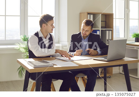 Two confident business men at work in office talking, reaching agreement and signing contract. Two confident business men at work in office talking, reaching agreement and signing contract. 135075027