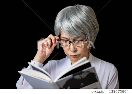老眼鏡をかけて本を読むシニア女性 135075904
