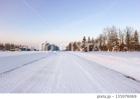 Plowed country road at the farm with granaries in winter. 135076069