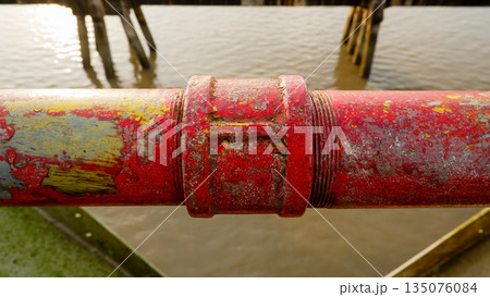 Close Up of Weathered Red Metal Railing Pipe with River Background 135076084