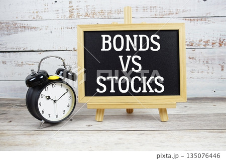 Bonds vs Stocks text written on blackboard with alarm clock on wooden background 135076446