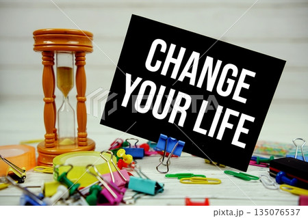 Change Your Life text on paper card with hourglass and stationary on wooden background 135076537