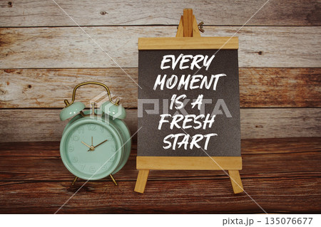 Every Moment Is A Fresh Start text on easel blackboard with alarm clock on wooden background 135076677