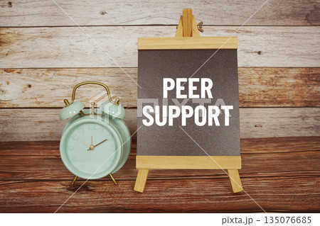 Peer Support text on easel blackboard with alarm clock on wooden background Peer Support text on easel blackboard with alarm clock on wooden background 135076685