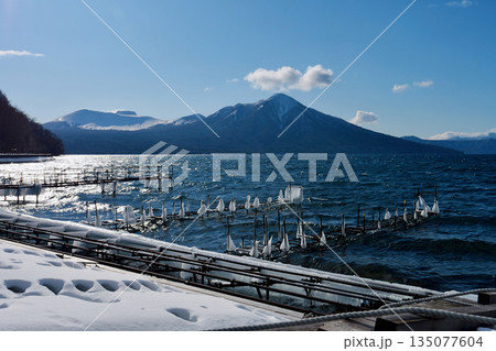 「1月の支笏湖」凍った桟橋に打ち寄せる波　奥に雪をまとった「風不死岳」 135077604