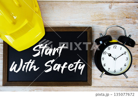 Start With Safety text written on blackboard with safety helmet and alarm clock on wooden background 135077672