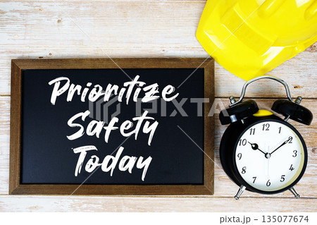 Prioritize Safety Today text written on blackboard with safety helmet and alarm clock on wooden background 135077674