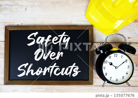 Safety Over Shortcuts text written on blackboard with safety helmet and alarm clock on wooden background 135077676