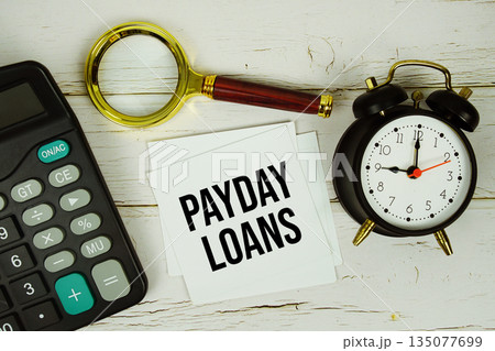 Payday Loans text with calculator, magnifying glass and alarm clock on wooden background 135077699