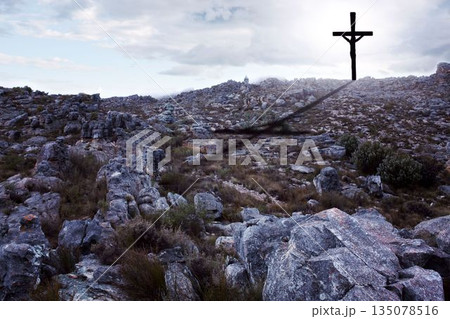 Rugged rocky hillside is showing in flat design with solitary cross casting shadow under cloudy sky 135078516