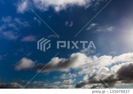 Cloud formations are drifting across deep blue sky in flat design with sunlight glare 135078837