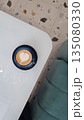Overhead view of a heart shaped latte art in a ceramic cup on a modern white table with terrazzo flooring and soft seating.  135080330