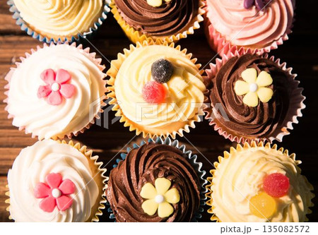 Nine cupcakes are sitting in flat design on wood tabletop with pastel liners and candy decorations 135082572