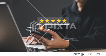 Close-up of hand holding smartphone with five-star rating icon, showing positive customer feedback, online review and digital satisfaction on mobile platform, concept of user experience. 135082968