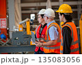 Three industrial engineers wearing safety uniform walk and discuss operations inside heavy factory, representing leadership, teamwork, and communication in high-risk industrial. 135083056