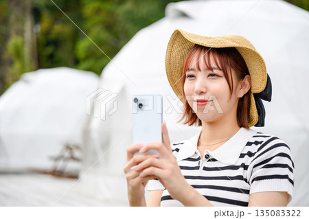 ドームテント前でスマホ撮影する女性 【撮影協力：隠岐シーサイドリゾートみやび様】 135083322