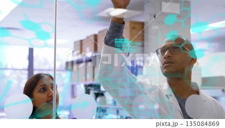 Collaborating scientists marking glass board at research lab, with turquoise digital graphics 135084869