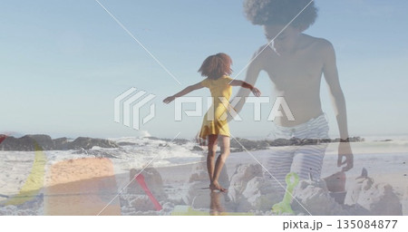 Twirling woman wearing yellow sundress balancing on sandy shore, with child sculpting sandcastle 135084877