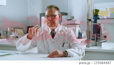 Senior scientist in lab coat pointing upward in research laboratory, with tablet computer on bench Senior scientist in lab coat pointing upward in research laboratory, with tablet computer on bench 135084887