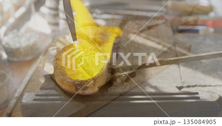 Pouring yellow molten metal stream from torch onto mold at metal workshop, with red-handle hammer 135084905