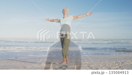 Standing senior woman stretching arms at sandy beach, with kneeling silhouette overlay Standing senior woman stretching arms at sandy beach, with kneeling silhouette overlay 135084913