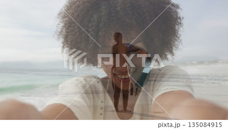 Extending arms taking selfie at beach woman in white tee overlaying couple walking with surfboard 135084915