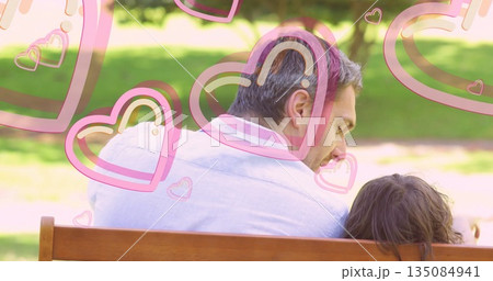Sitting father and son sharing moment on wooden park bench, with translucent pink heart graphics 135084941