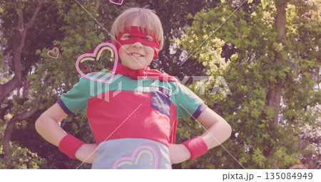 Boy in superhero costume standing in backyard garden, with red mask cape wristbands and pink hearts Boy in superhero costume standing in backyard garden, with red mask cape wristbands and pink hearts 135084949