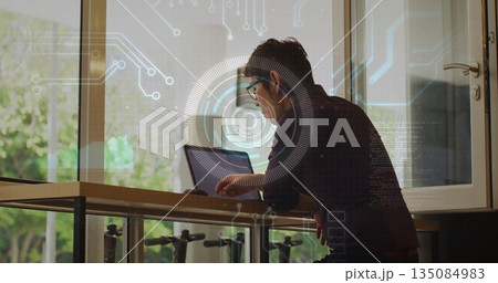 Leaning man in collared shirt using laptop at office standing desk with digital overlay, copy space Leaning man in collared shirt using laptop at office standing desk with digital overlay, copy space 135084983