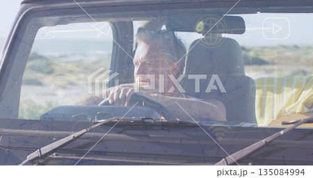 Gripping steering wheel mature adult man gazing through windshield at coastal dunes, dashboard 135084994