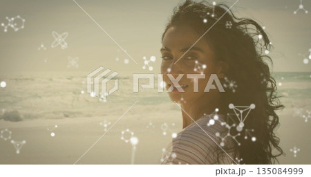 Standing Latina in striped T-shirt looking back on beach showing molecular overlays, copy space 135084999