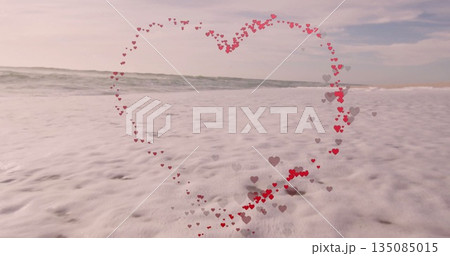 Clustering small red and gray heart shapes forming heart outline at shoreline, with ocean waves 135085015