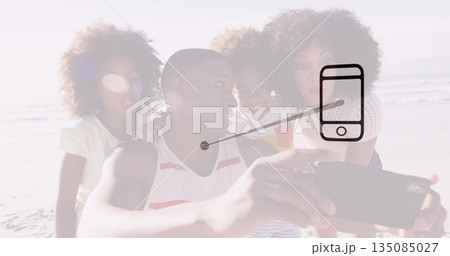 Family of four taking selfie on sandy shoreline at water's edge, with smartphone lens flare 135085027