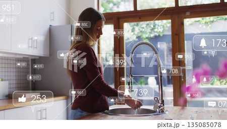 Woman rinsing dishes under pull-down faucet at kitchen sink with social media overlays, copy space 135085078