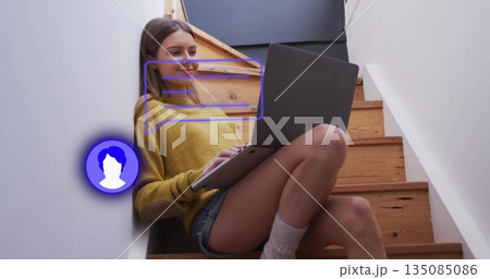 Sitting woman wearing mustard sweater, denim shorts on wood stairs at home, holding laptop computer 135085086