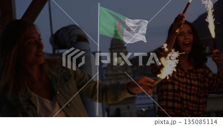 Waving two women holding sparklers on rooftop terrace at dusk, with Algerian flag fluttering Waving two women holding sparklers on rooftop terrace at dusk, with Algerian flag fluttering 135085114