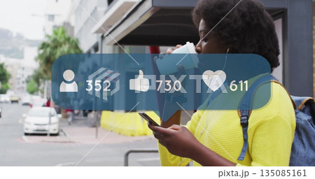 Holding coffee cup and scrolling smartphone on city sidewalk with earbuds and backpack, copy space 135085161