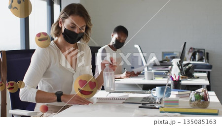 Office worker spraying and wiping desk at open-plan workspace, with spray bottle and cloth 135085163