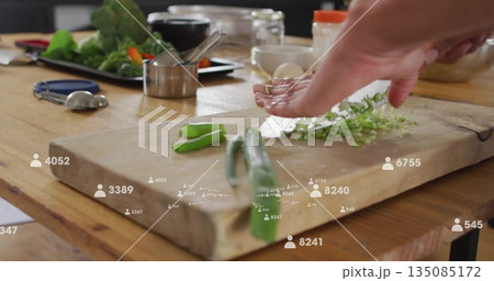 Chopping adult woman preparing herbs with knife on wooden cutting board, floating follower icons 135085172