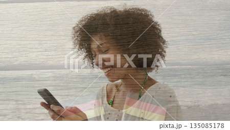 Smiling woman standing at seaside beach, using smartphone and showing green swimsuit straps 135085178
