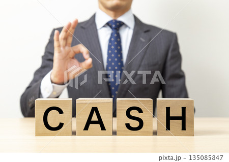 「CASH」と書かれたブロックとOKポーズをするビジネスマン 「CASH」と書かれたブロックとOKポーズをするビジネスマン 135085847