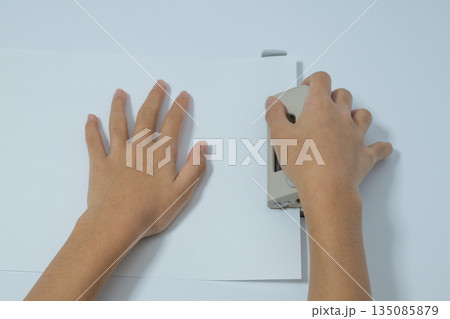 紙にパンチで穴をあける子供の手元の真上俯瞰 紙にパンチで穴をあける子供の手元の真上俯瞰 135085879
